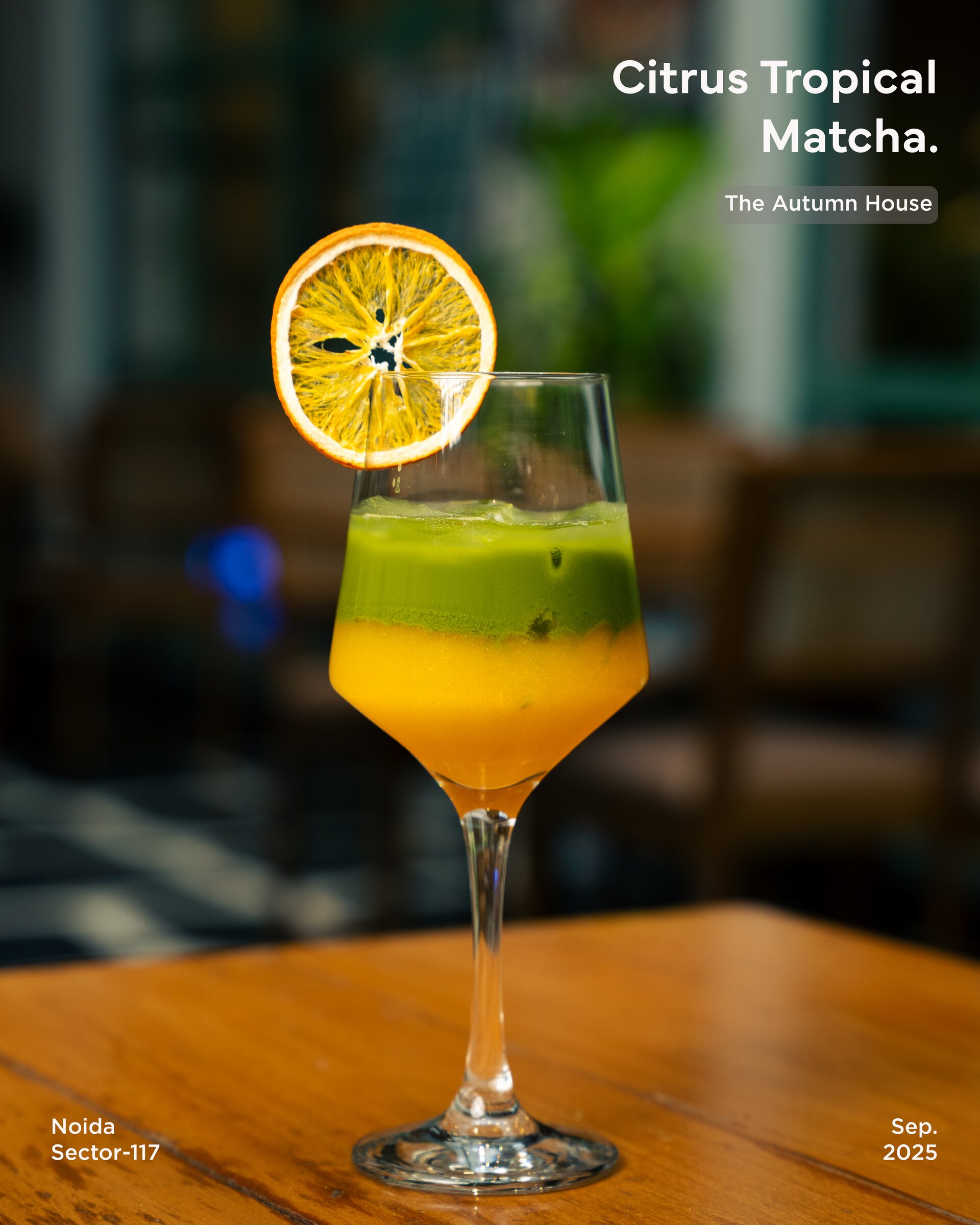 A layered citrus tropical matcha with a dried orange wheel on a wooden table