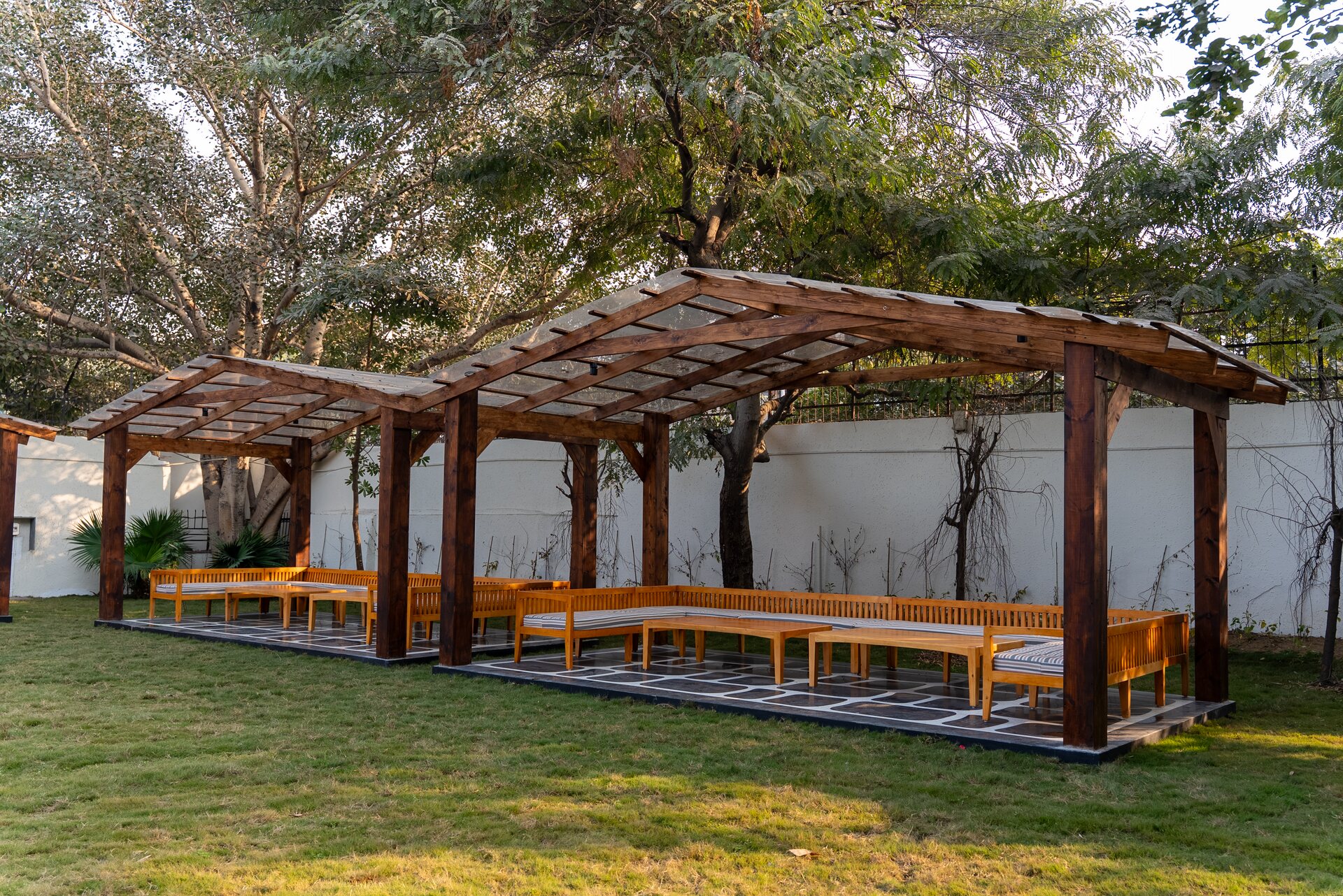 A timber pergola with long benches on a lawn under tall trees
