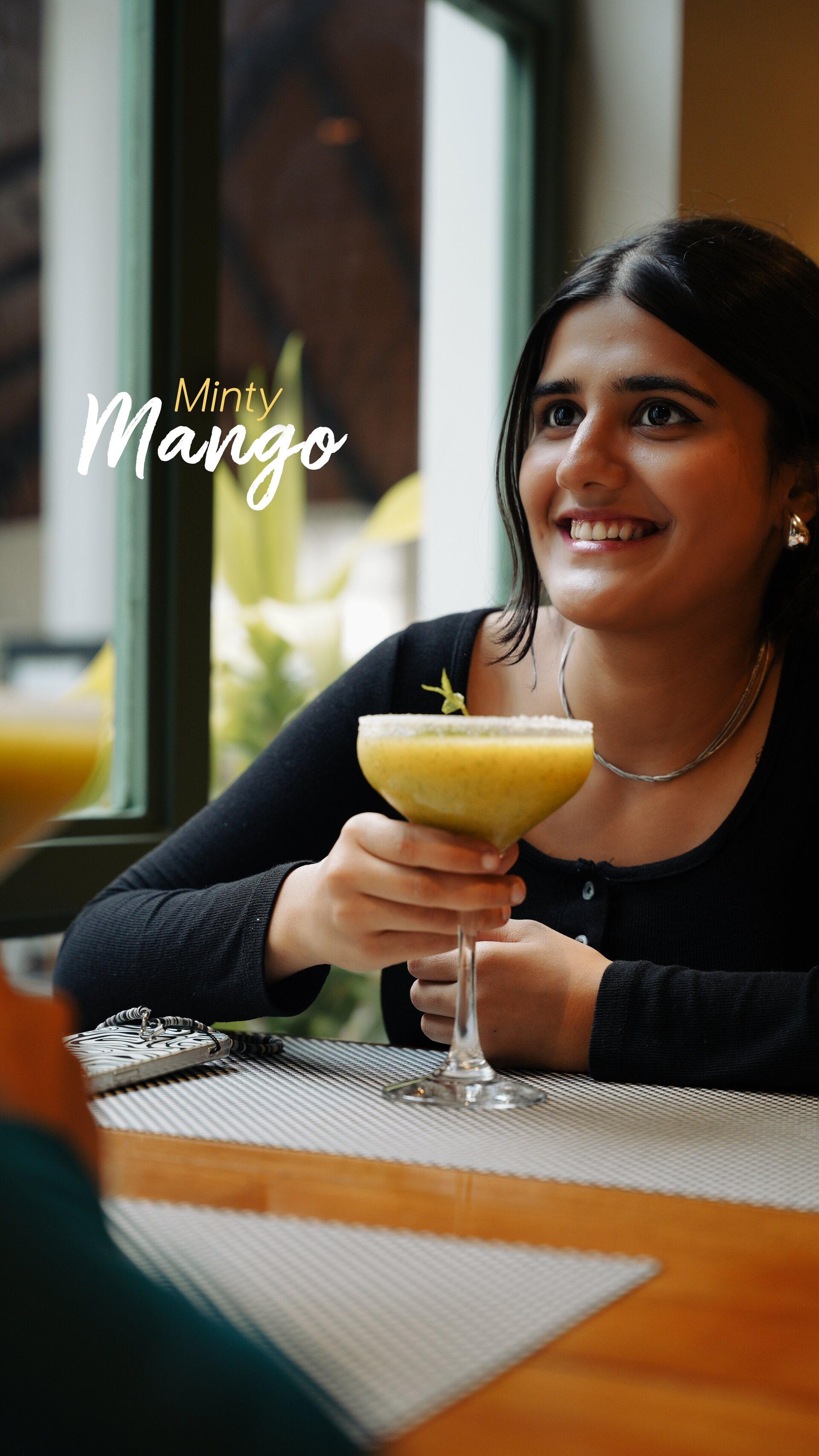 A smiling guest raising a minty mango drink by the window