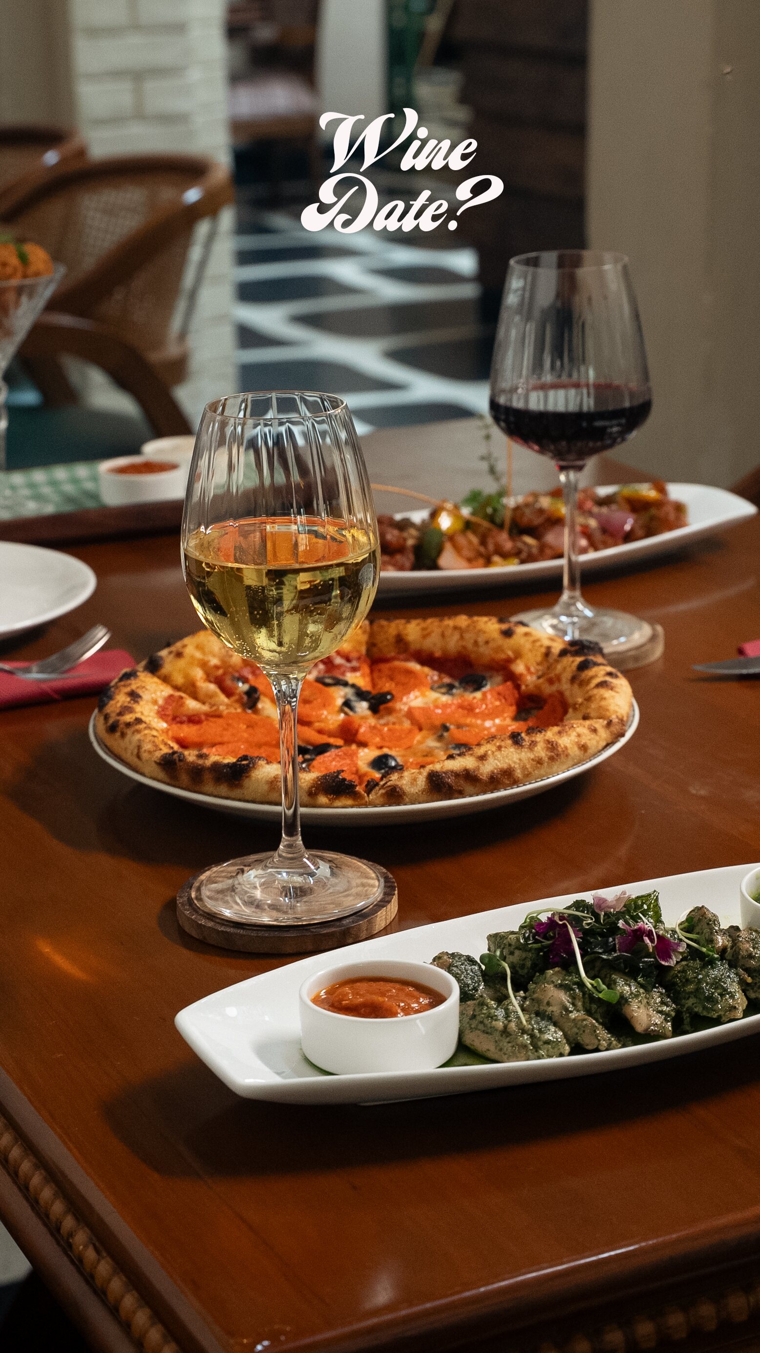 Wood-fired pizza, a dip and two glasses of wine on a dark wooden table